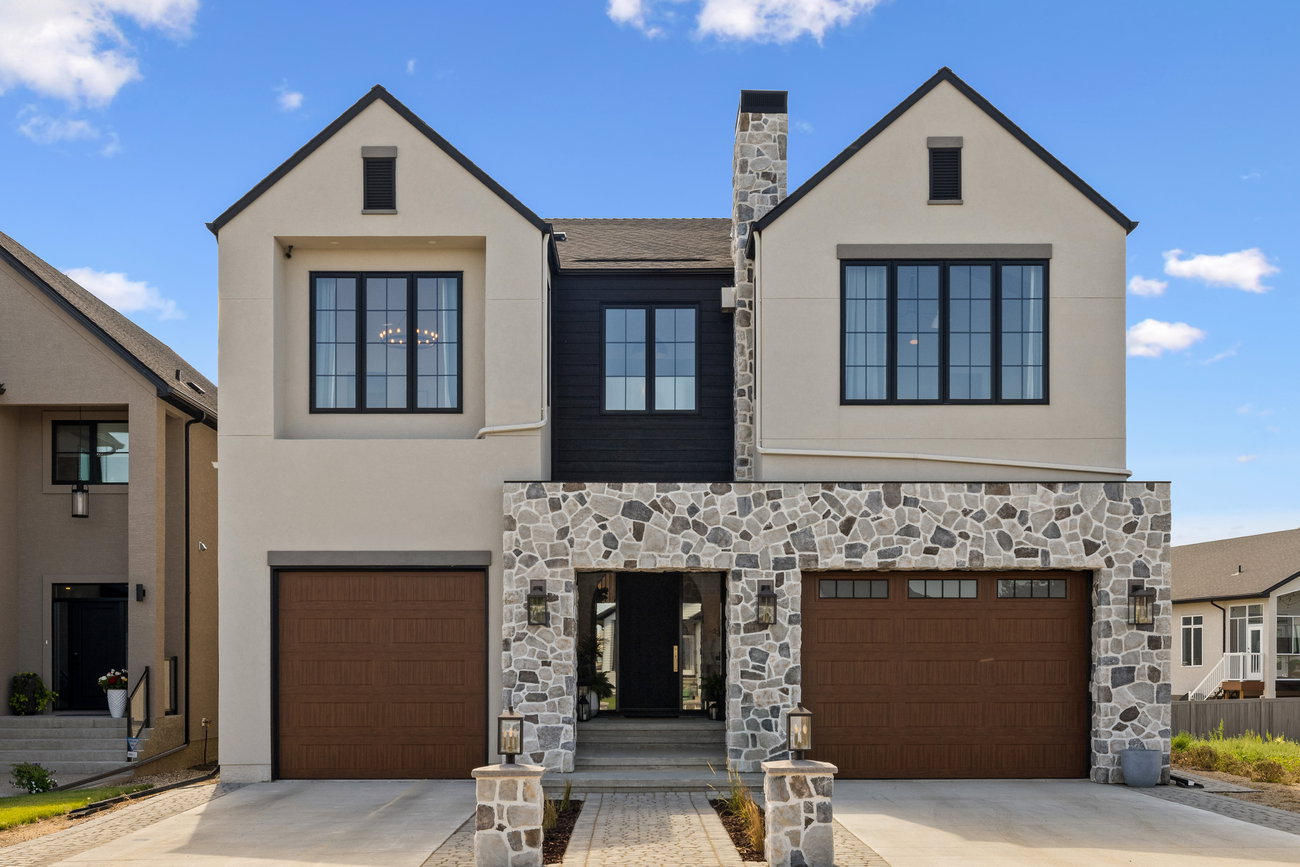 Two-storey home exterior with light stone and wood siding, framed by mature trees