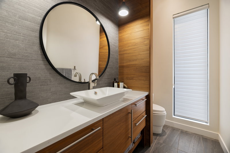 Main floor bathroom with mosaic tile and a round black-framed mirror