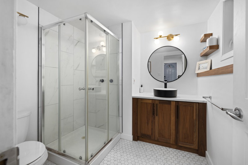 Second bathroom with a corner glass shower and round black-framed mirror