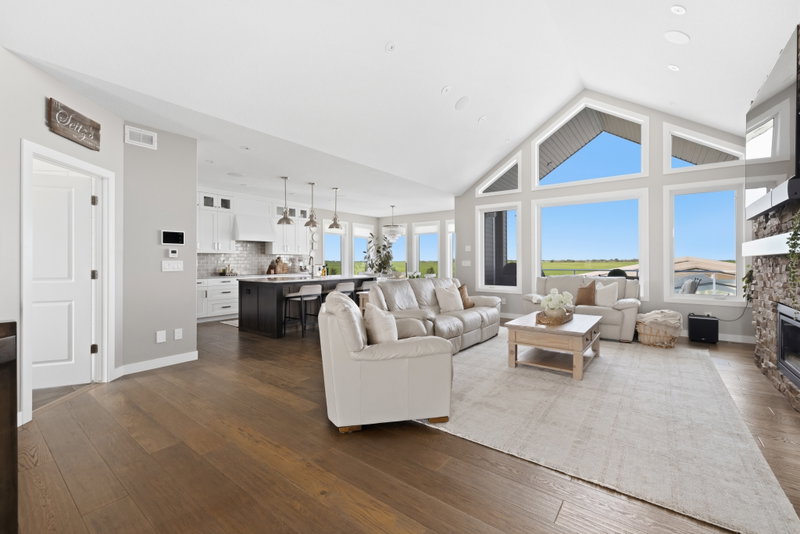 Open-concept living room and kitchen beneath a vaulted ceiling with floor-to-ceiling windows